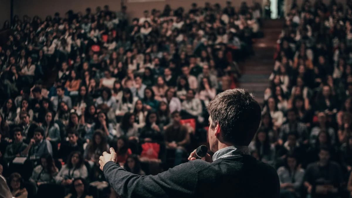 A speaker addressing a full auditorium from a lit stage