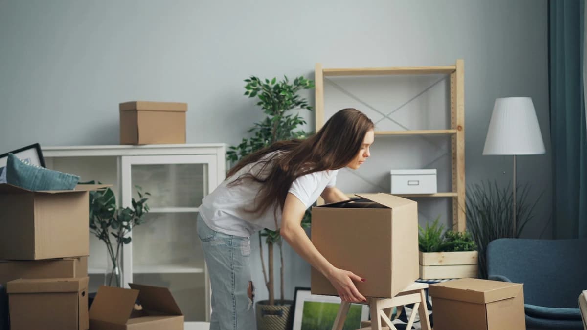 A woman moving boxes through a bare living room