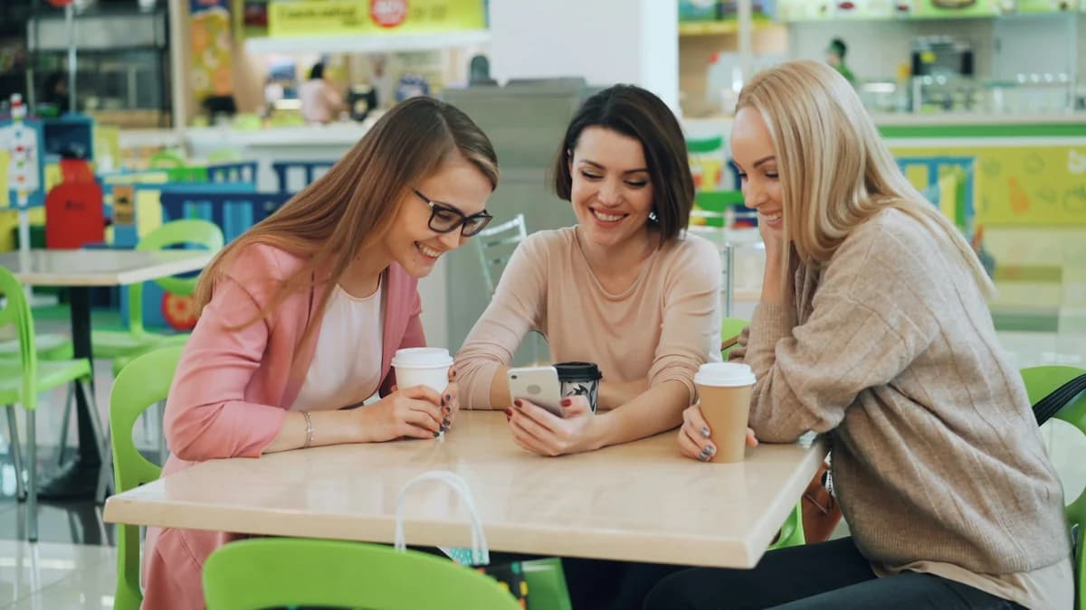 Three friends at a cafe table laughing at a phone