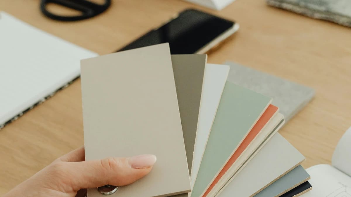 A hand holding colour swatches over a desk of proofs